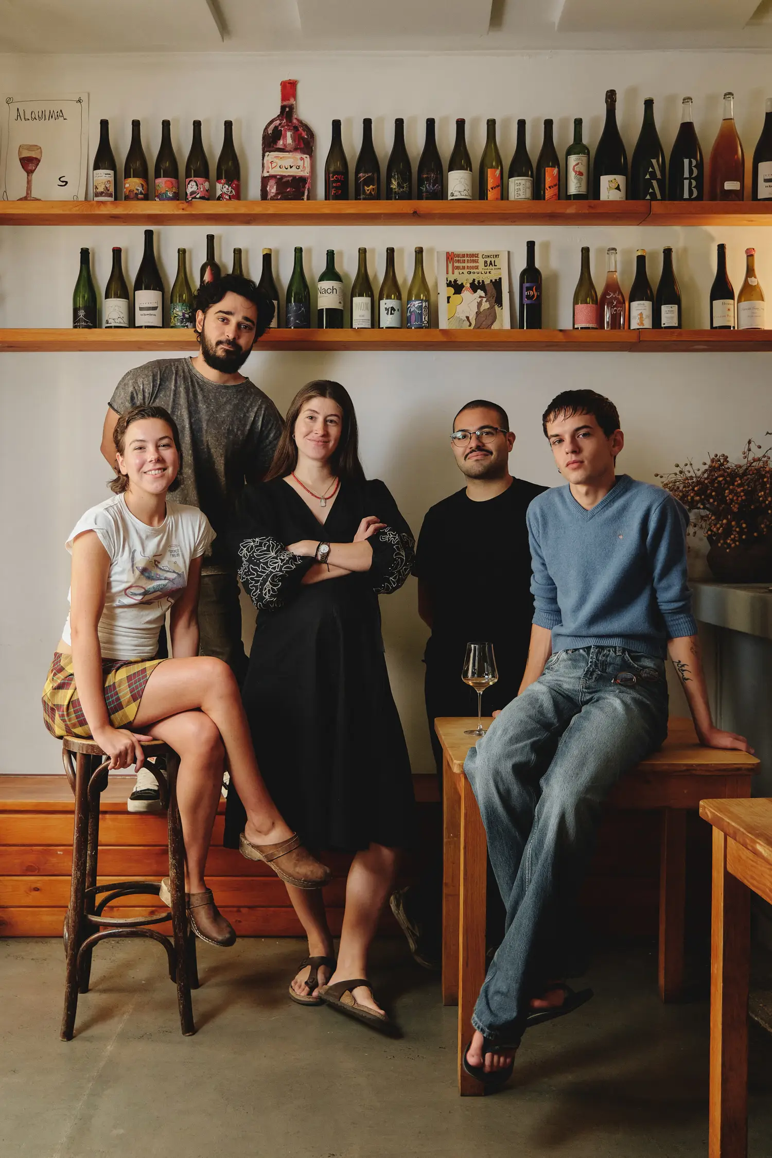 Un grupo de amigos sonríe en un ambiente relajado, rodeados de estanterías repletas de botellas de vino en un local acogedor.