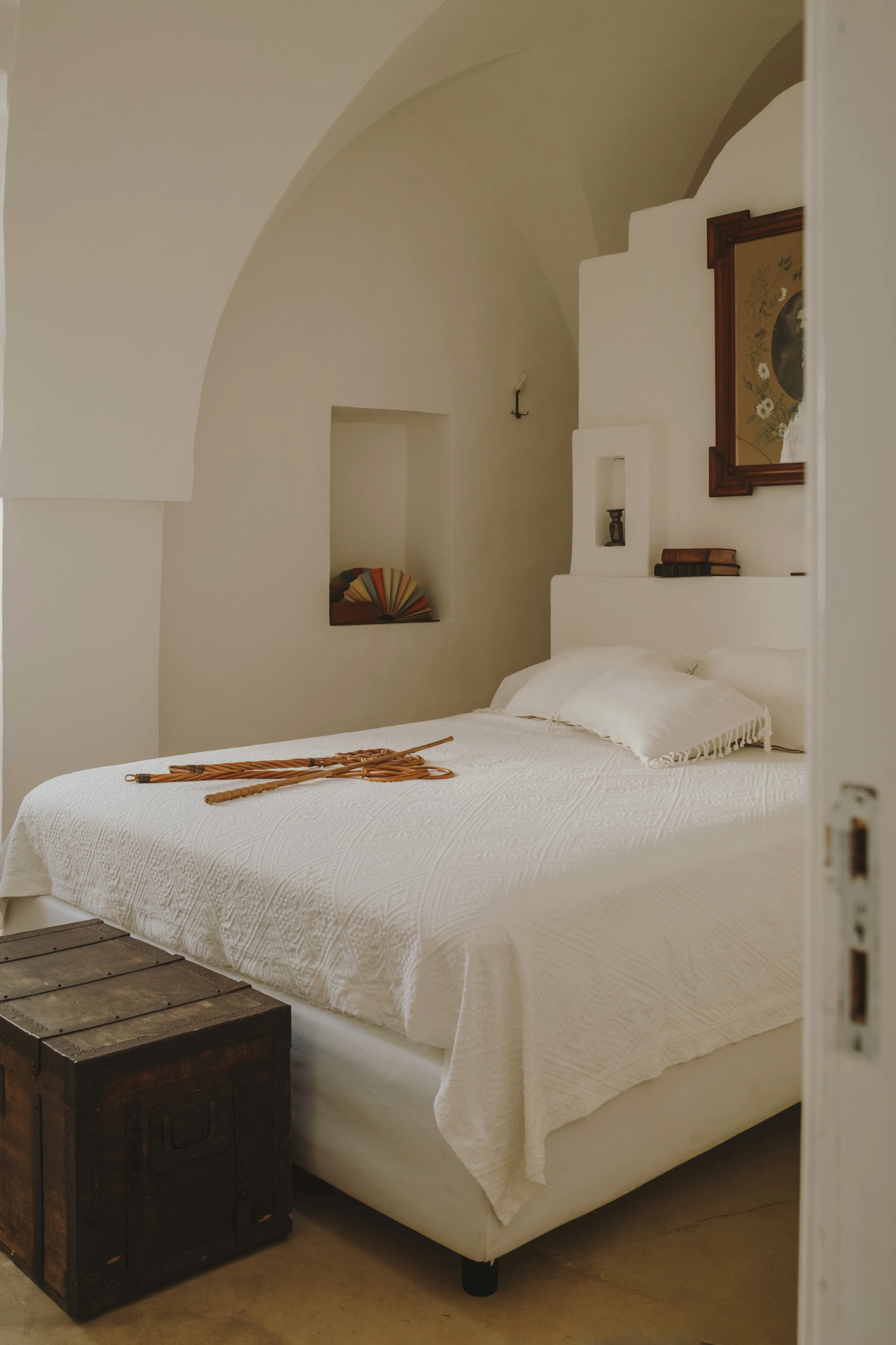 Espacioso dormitorio en tonos claros con techos abovedados, una cama blanca y detalles rústicos mediterráneos.