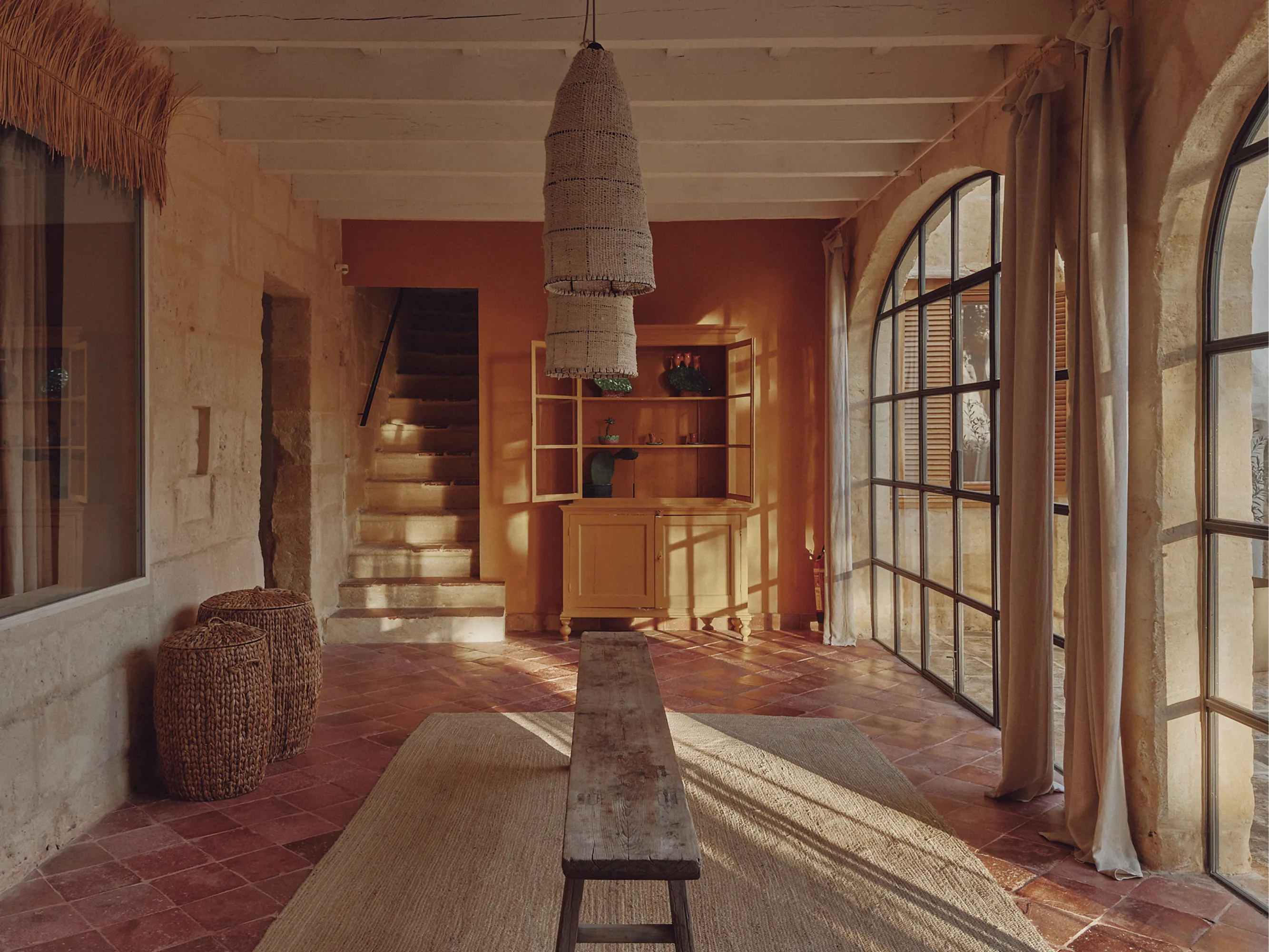 Espacioso interior mediterráneo de inspiración rústica con paredes de piedra, arcos, suelo de terracota y luz cálida.