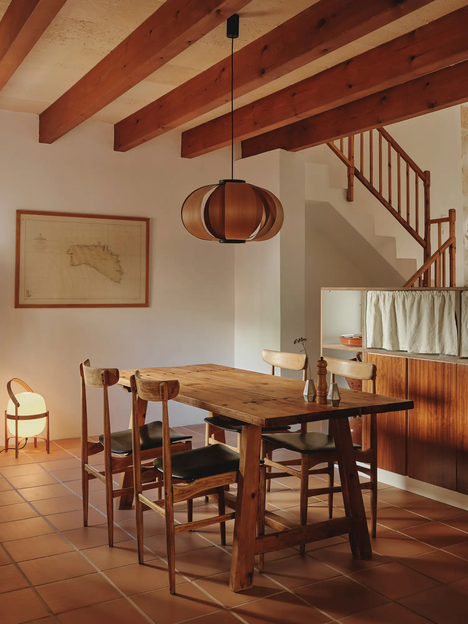 Comedor rústico mediterráneo con mesa de madera, sillas y lámpara de diseño bajo un techo con vigas vistas.