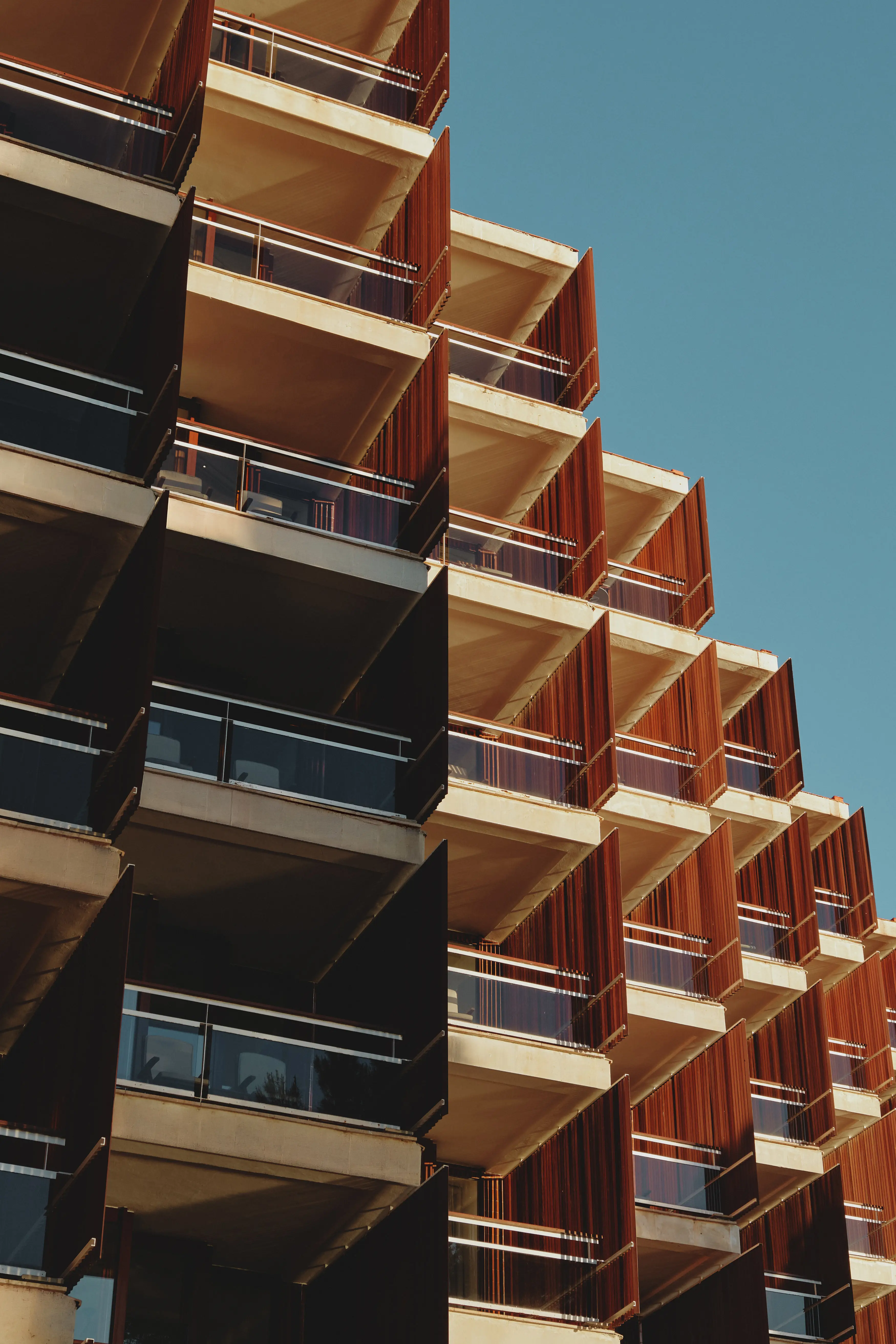 Diseño arquitectónico de balcones angulares en una fachada moderna con paneles de madera y barandillas de cristal bajo luz cálida.