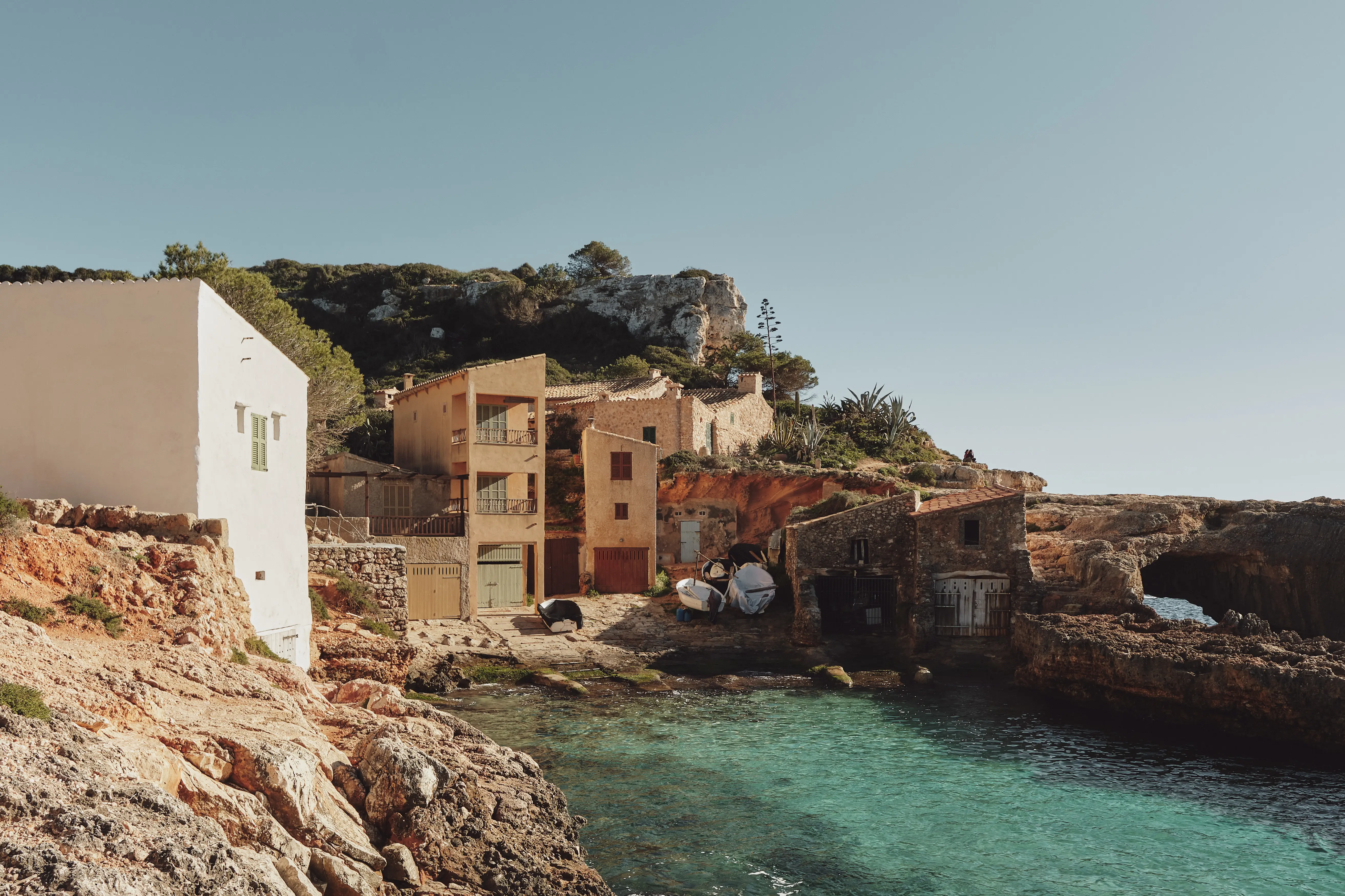 Casas mediterráneas encaladas y de tonos tierra se asientan sobre un acantilado rocoso junto a aguas turquesas.