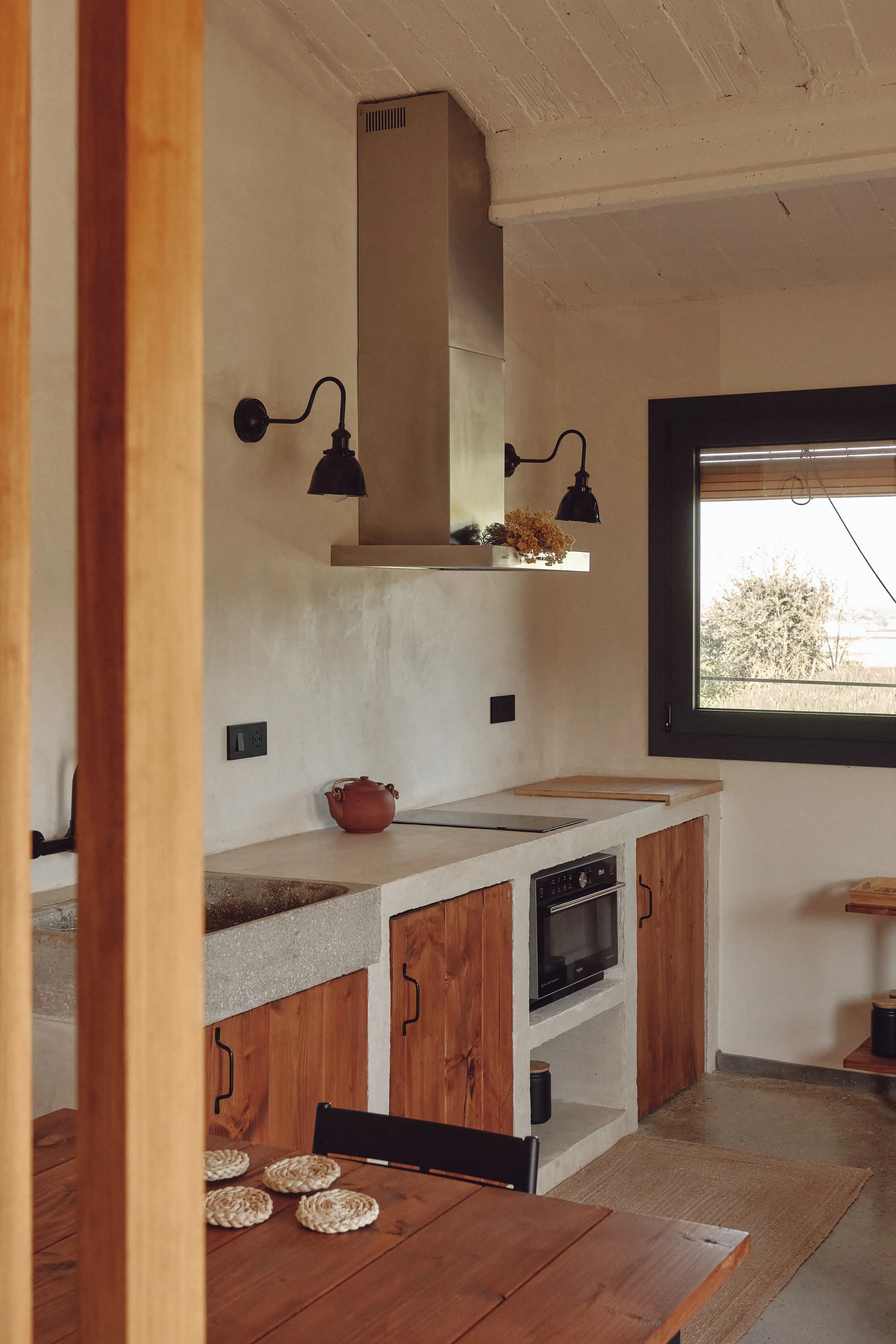 Cocina de diseño rústico-mediterráneo con encimeras de hormigón, detalles en madera y luz natural.