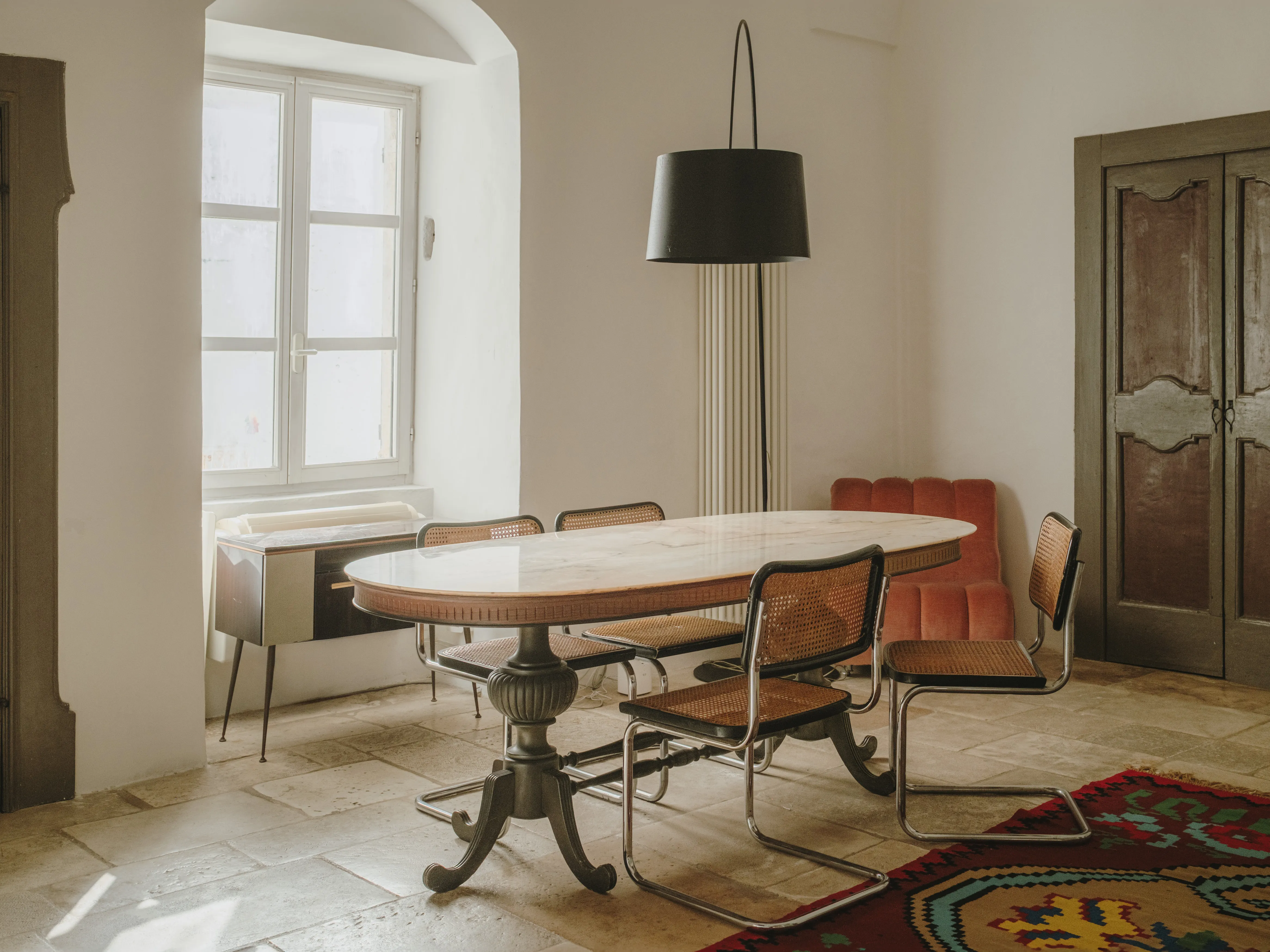 Comedor luminoso con mesa ovalada, sillas de diseño Cesca, lámpara colgante y un contraste de muebles clásicos y modernos.