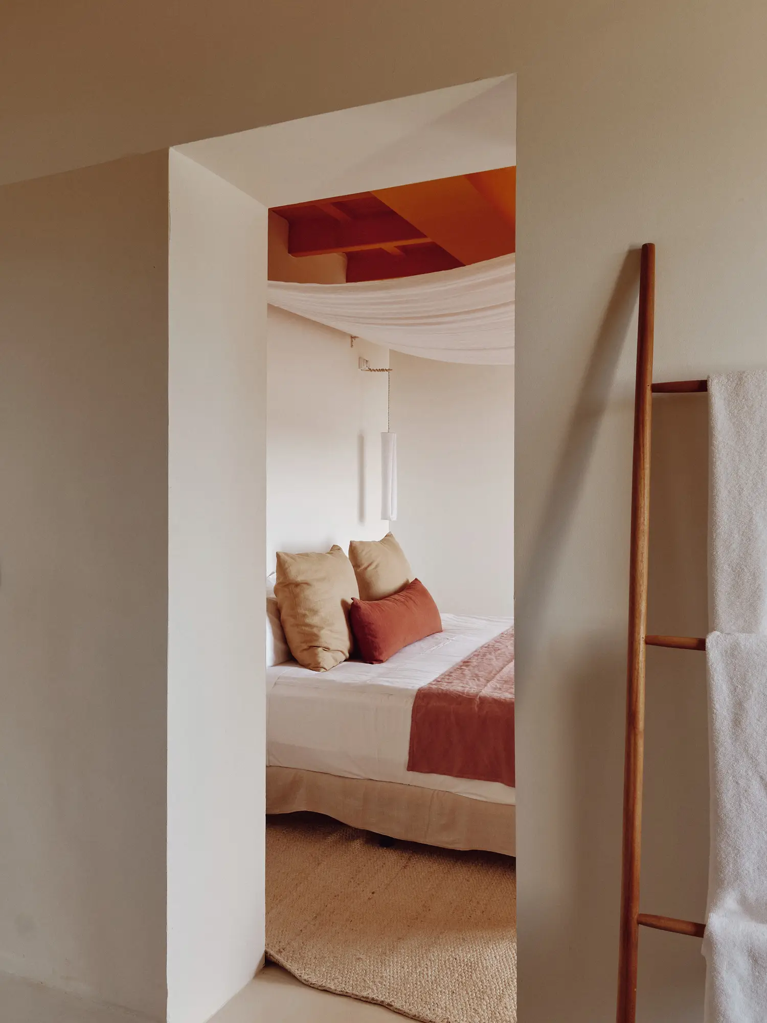 Dormitorio de estilo mediterráneo con cama vestida en tonos tierra, dosel de tela y techo con vigas de madera a la vista.