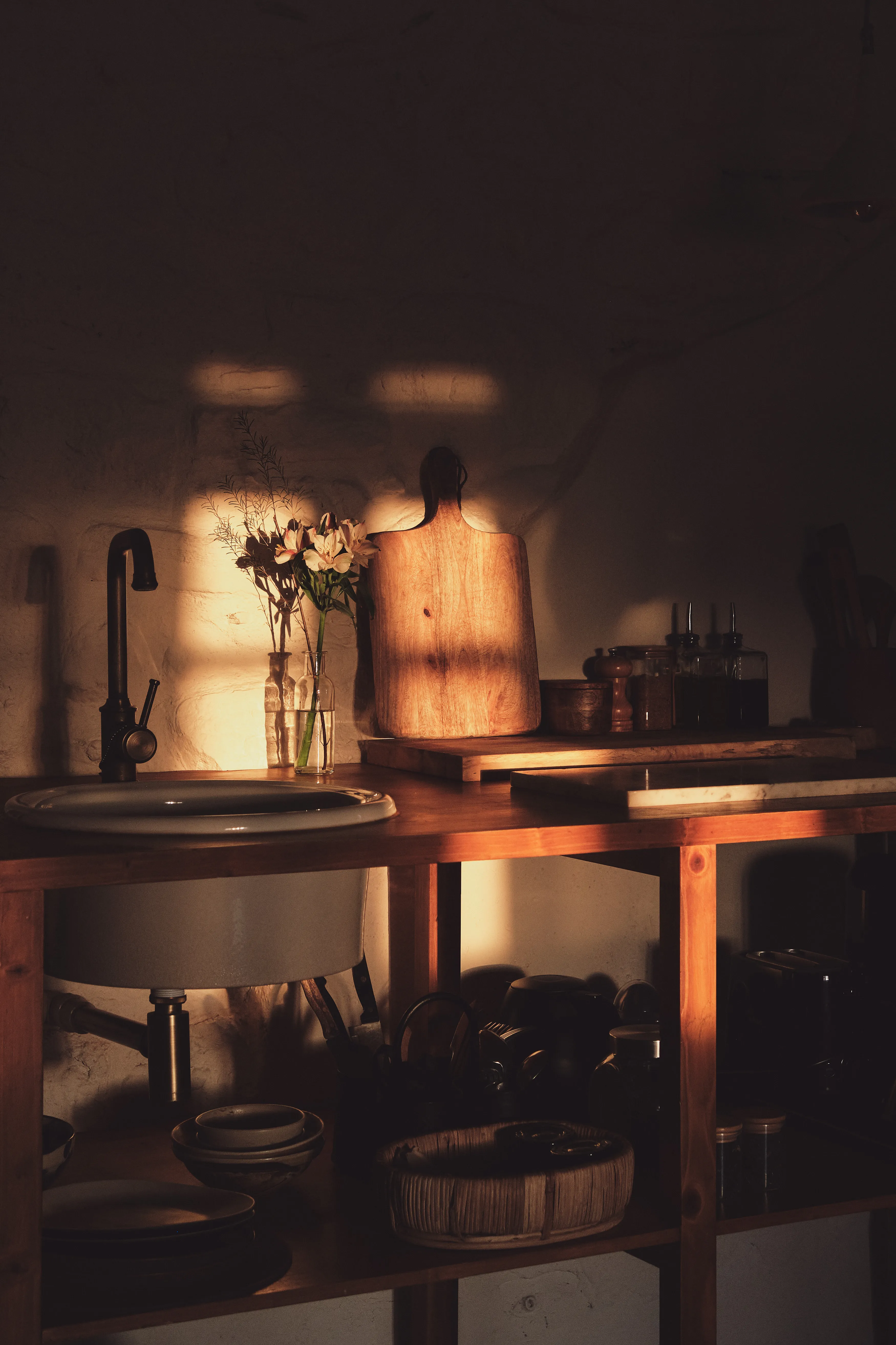 Cocina rústica bajo luz dorada de atardecer, destacando el fregadero, flores y tabla de cortar de madera.