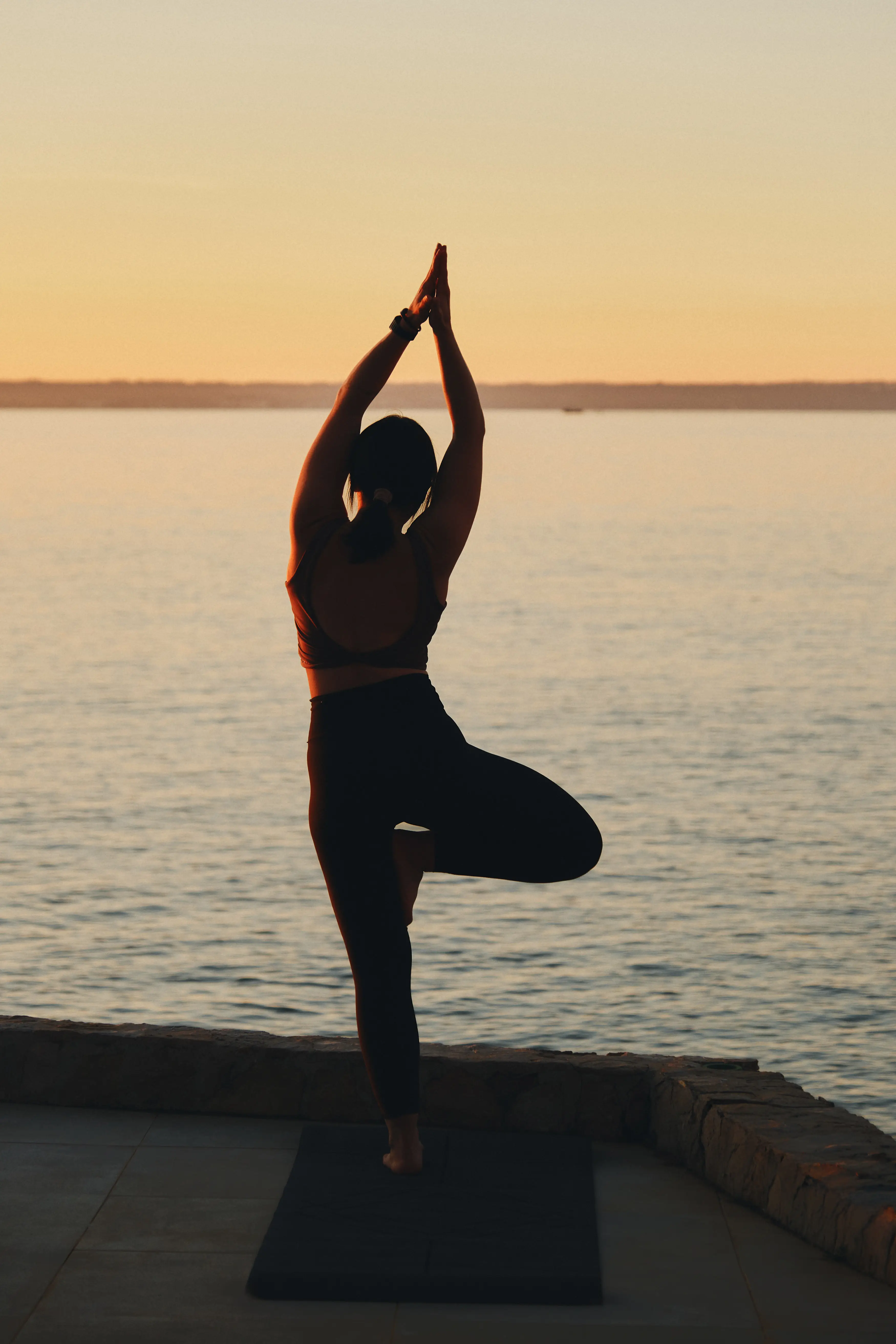 Silueta de una mujer practicando yoga al atardecer junto al mar, en una serena escena de bienestar y conexión.