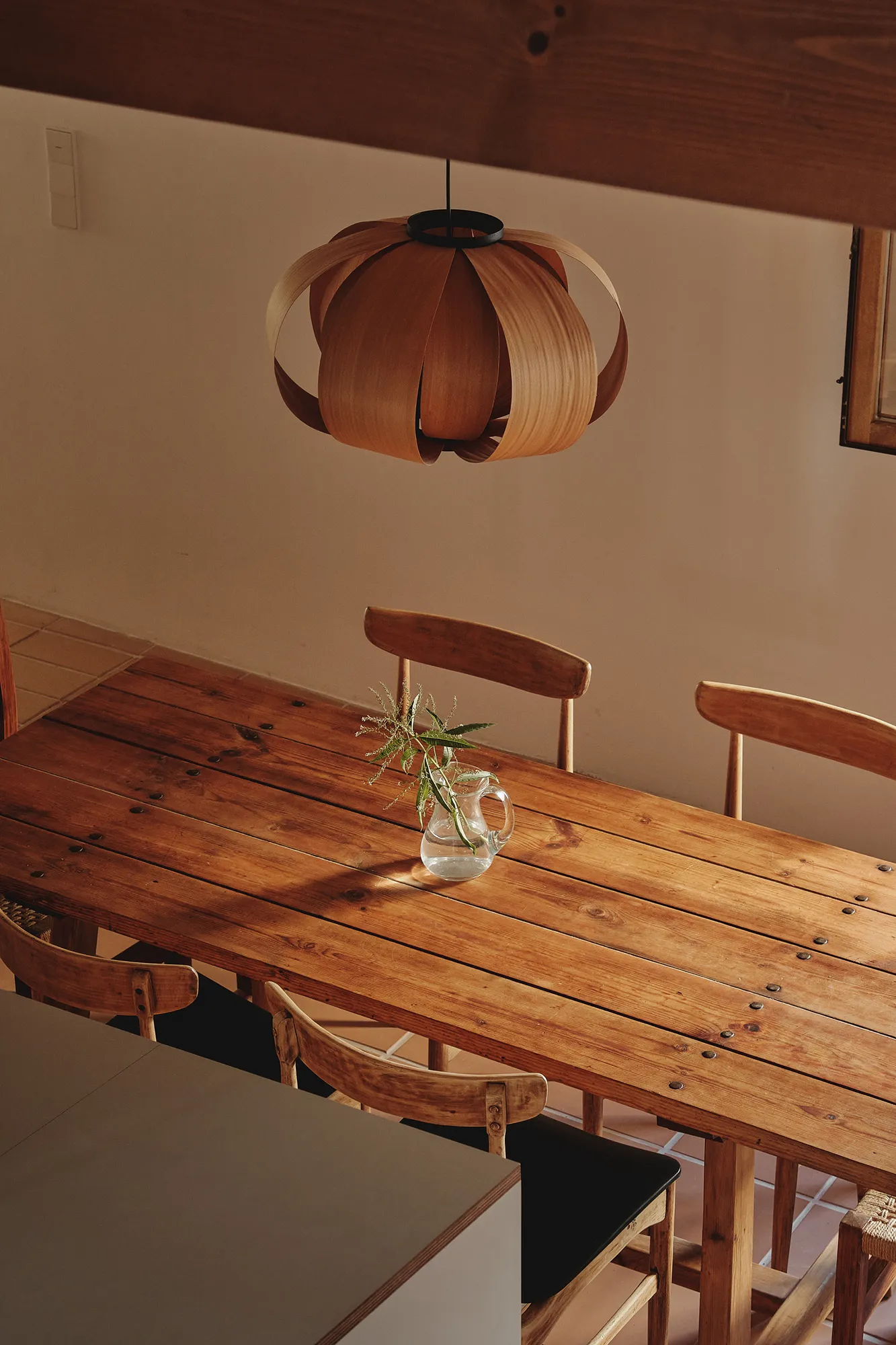 Mesa de comedor de madera rústica con sillas y una lámpara colgante de diseño, bañada por luz natural.