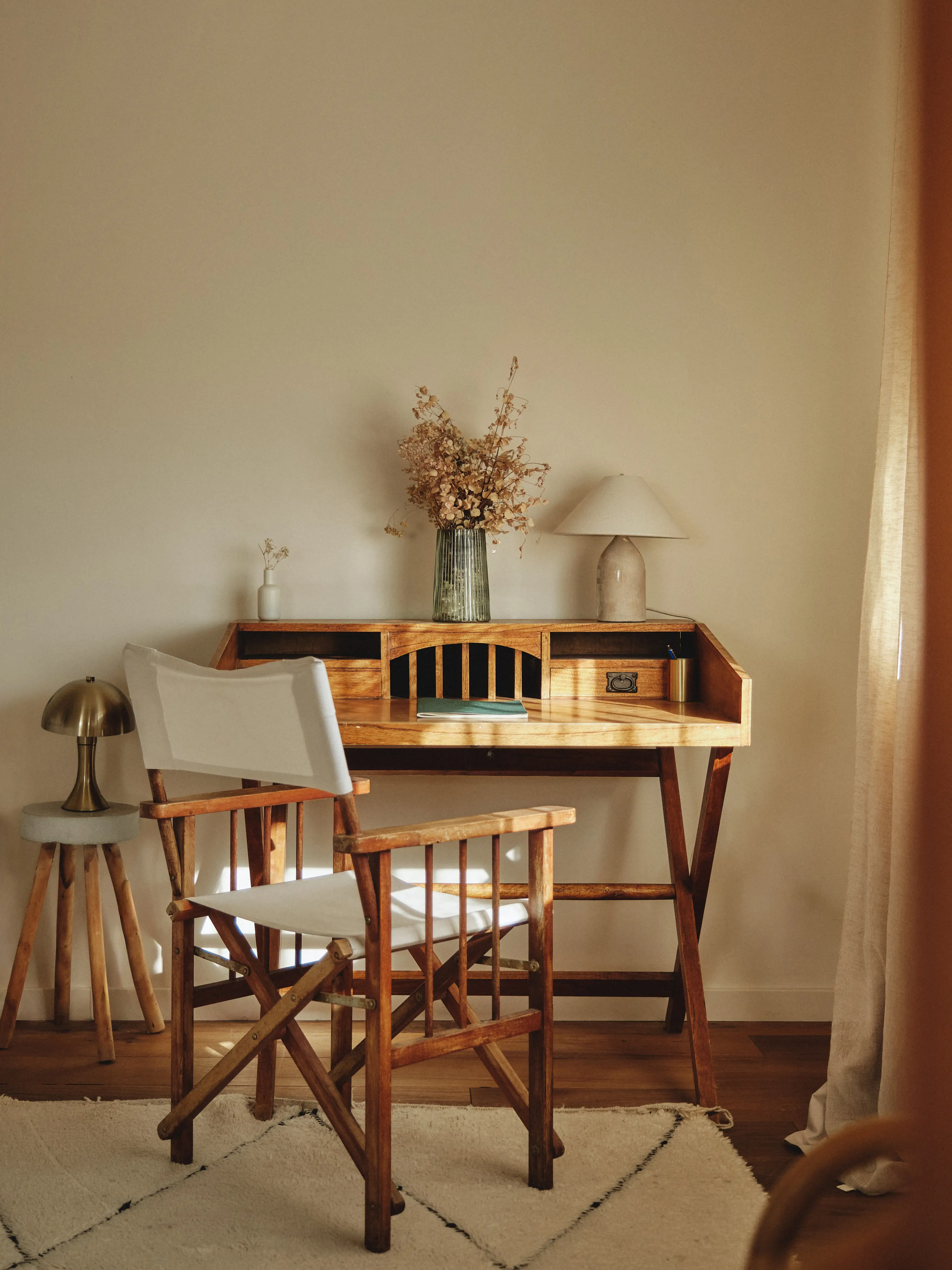 Rincón de estudio luminoso con escritorio de madera rústica, silla de director y detalles naturales como flores secas y lámparas.