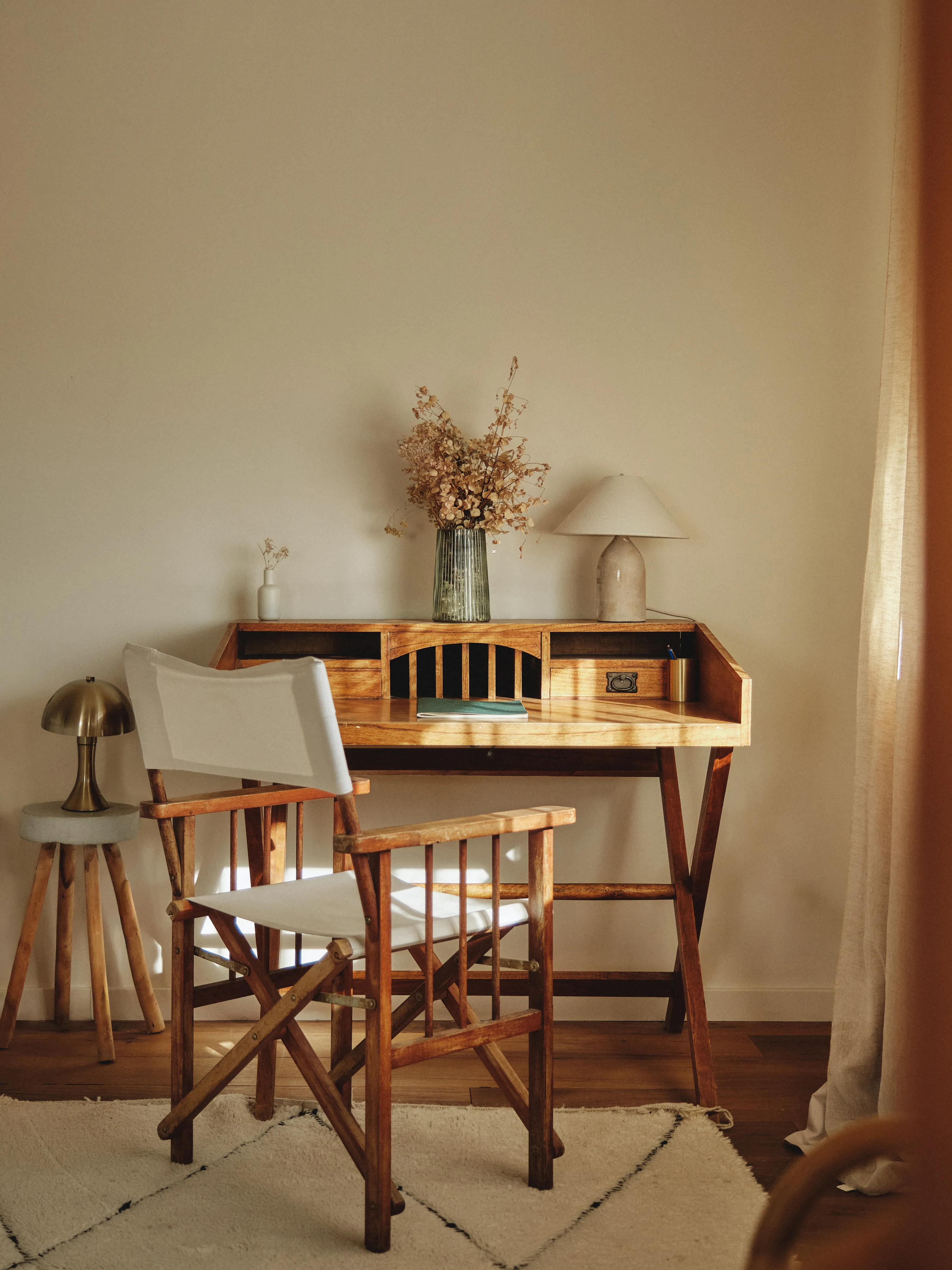 Rincón de estudio luminoso con escritorio de madera rústica, silla de director y detalles naturales como flores secas y lámparas.