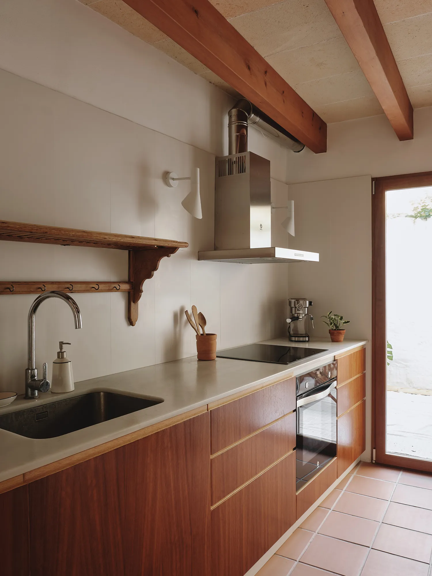 Cocina de estilo mediterráneo con vigas de madera, encimera clara y muebles de madera, abierta a un patio exterior.