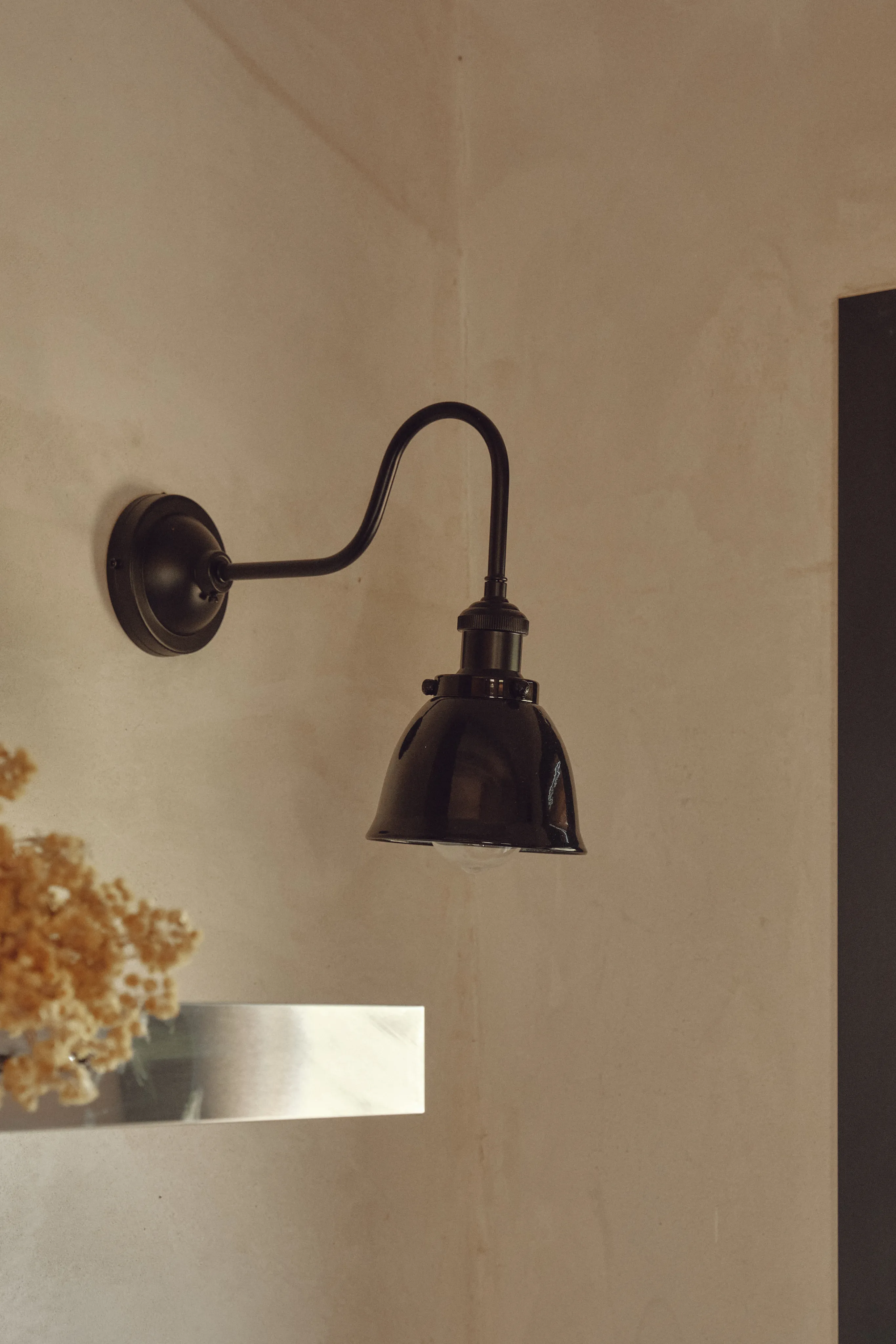 Aplique de pared negro tipo gooseneck sobre pared texturizada, creando un ambiente cálido y minimalista.