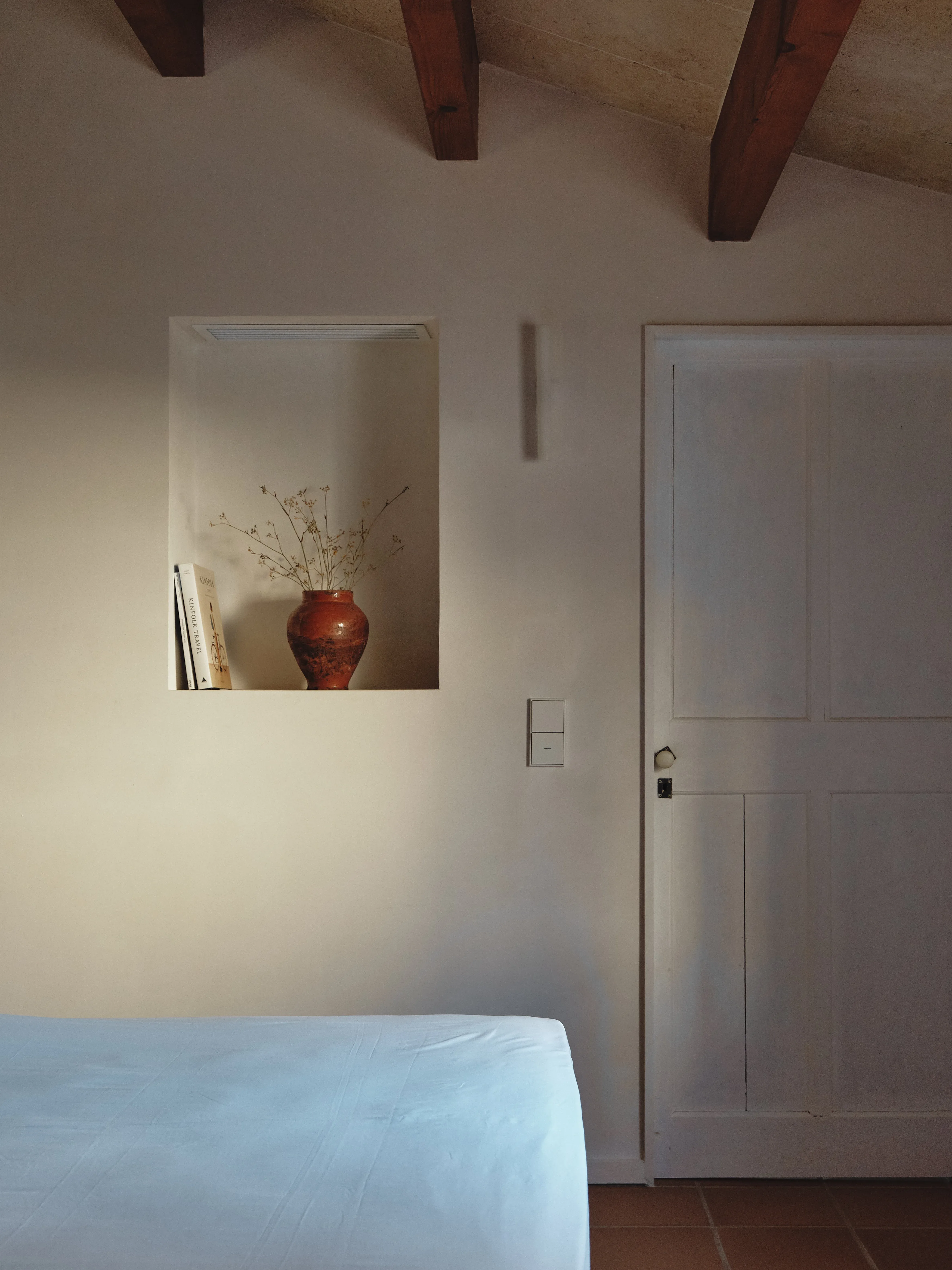 Interior acogedor con cama, nicho decorado con libros y jarrón, y detalles arquitectónicos en el techo.