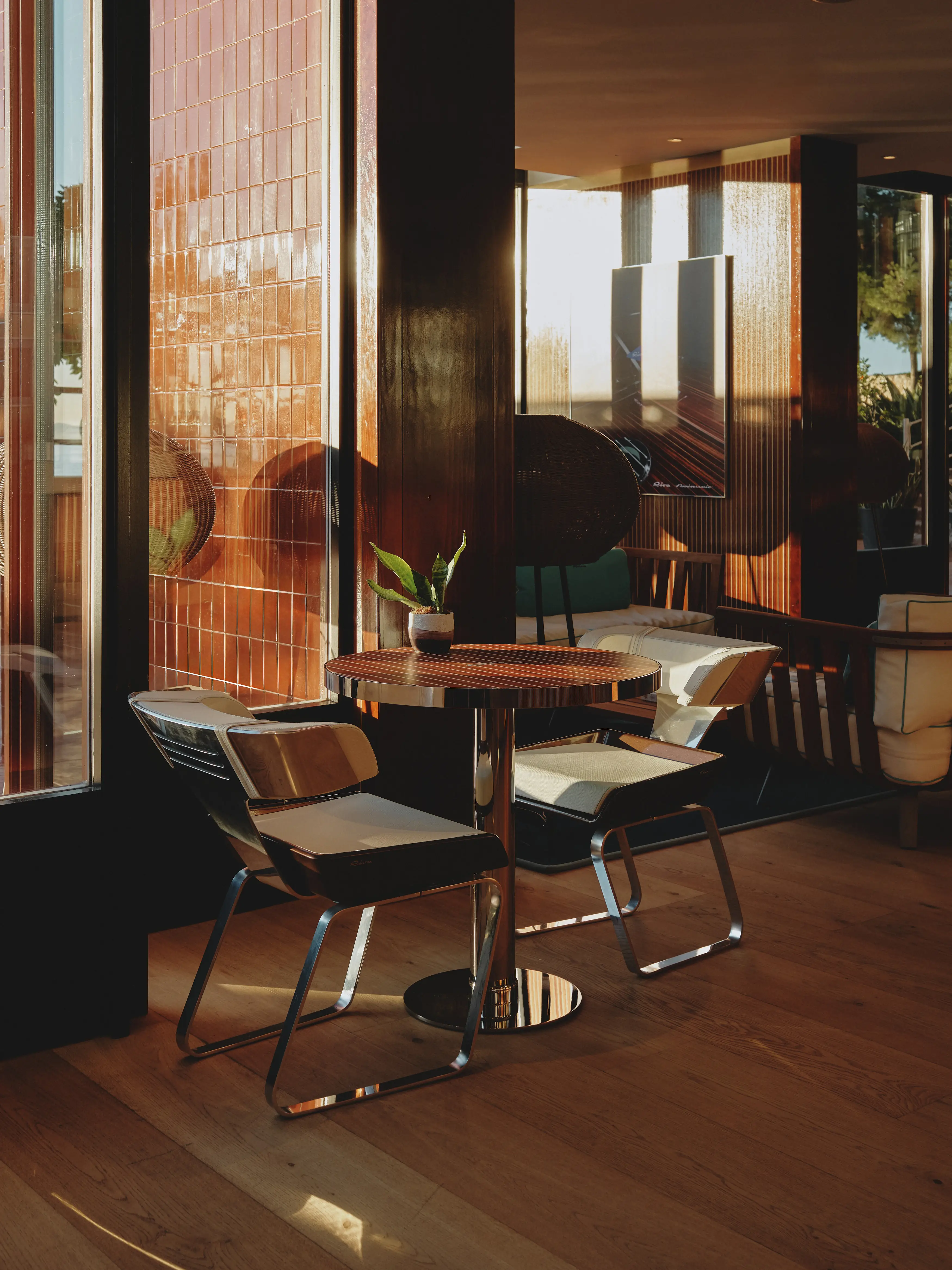 Espacio interior cálido con mesa redonda y sillas de diseño, iluminado por la luz del atardecer a través de una ventana con azulejos.