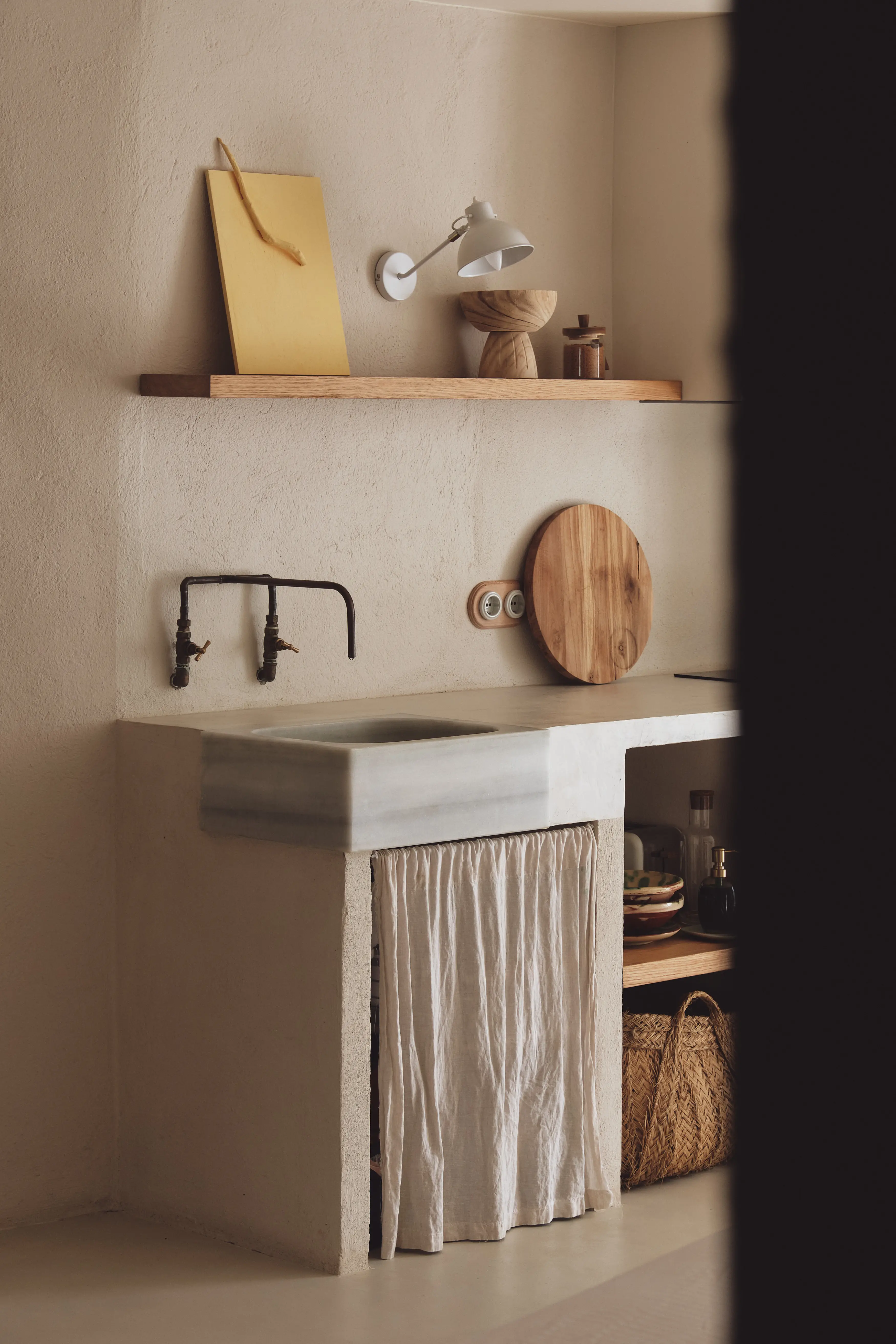 Cocina minimalista de inspiración mediterránea con fregadero de mármol, grifos de metal y estantería de madera.