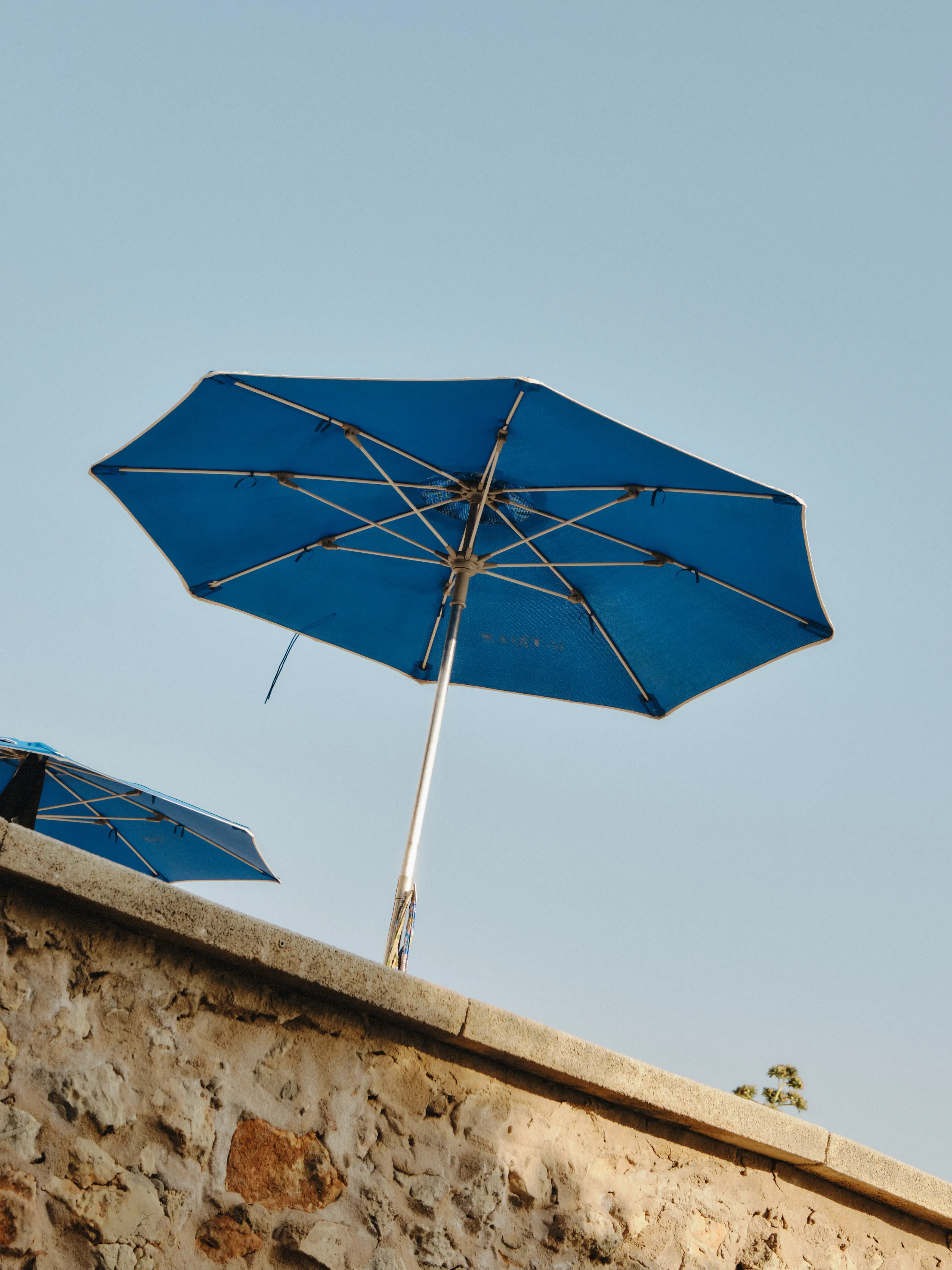 Sombrillas azules sobre un muro de piedra bajo el cielo despejado, un rincón de relax mediterráneo al aire libre.