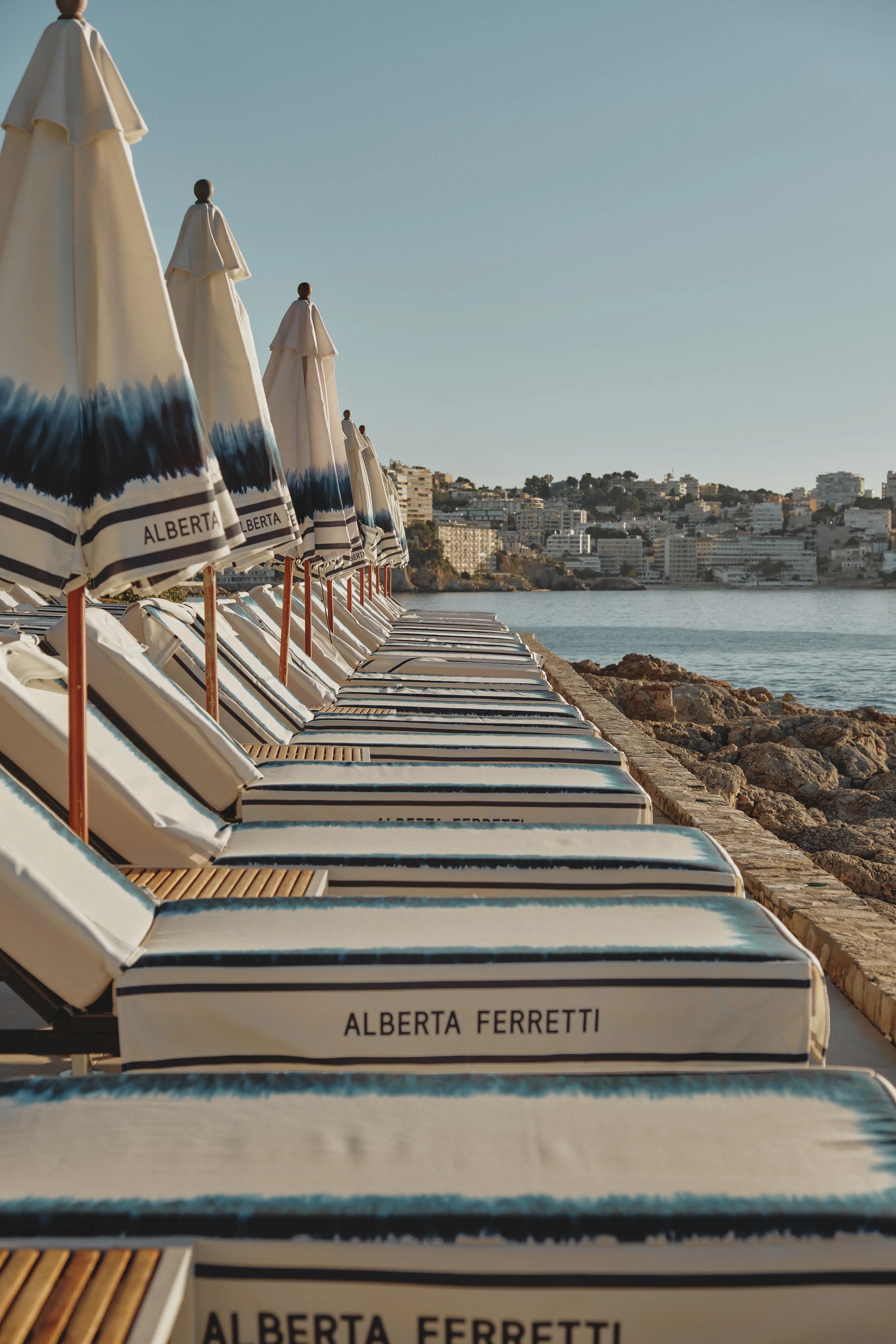 Sombrillas y tumbonas de diseño junto al mar, invitando a la relajación en un exclusivo resort mediterráneo.