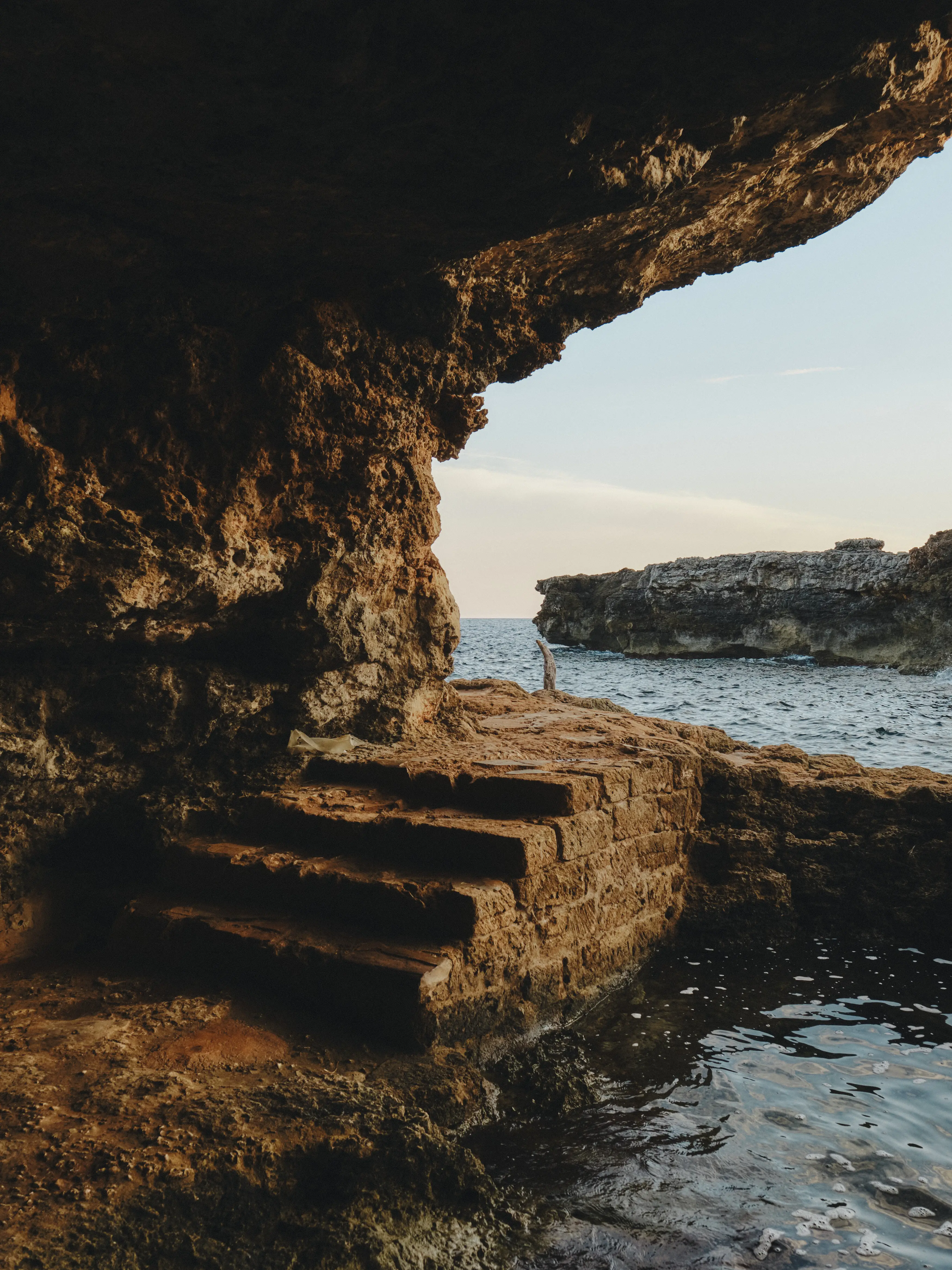 Escaleras de roca talladas en una cueva natural junto al mar Mediterráneo al atardecer.