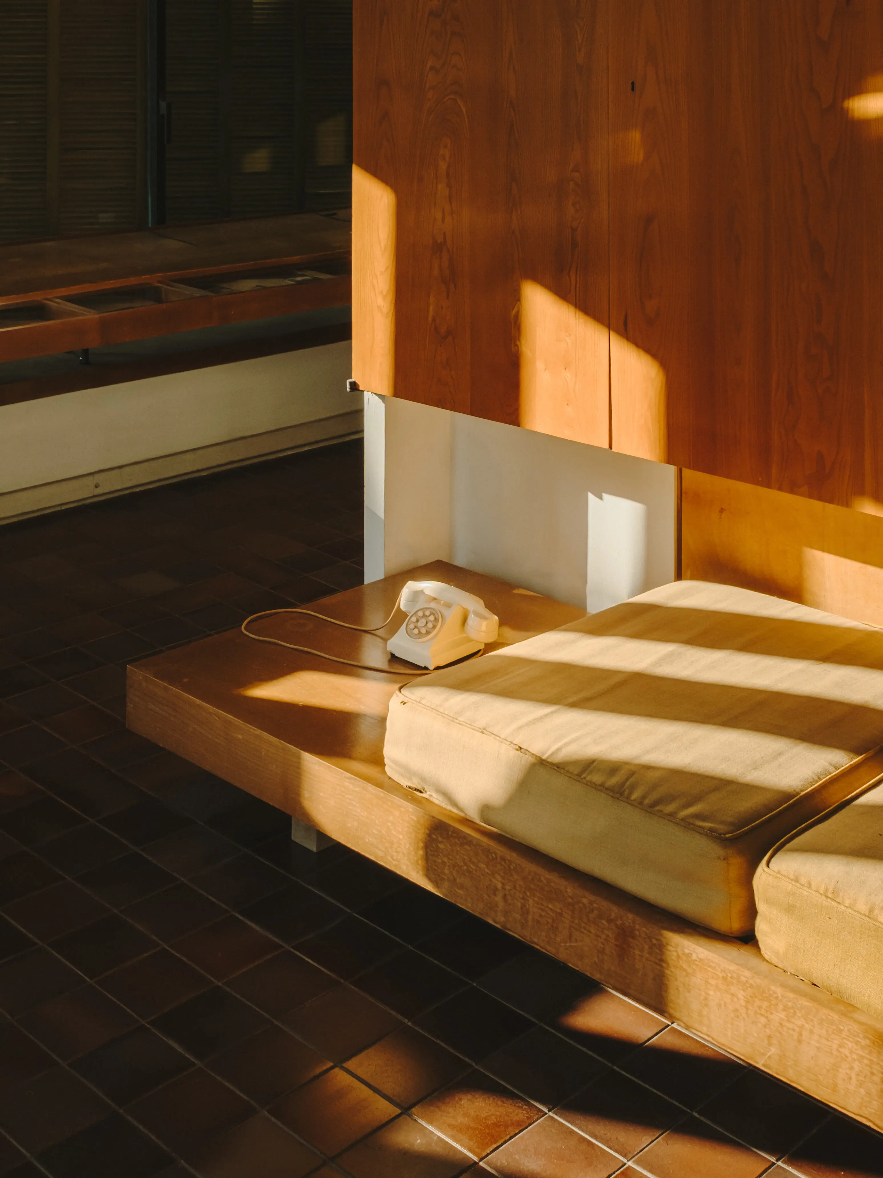 Luz cálida inunda un rincón acogedor con banco de madera, cojines claros y teléfono retro.