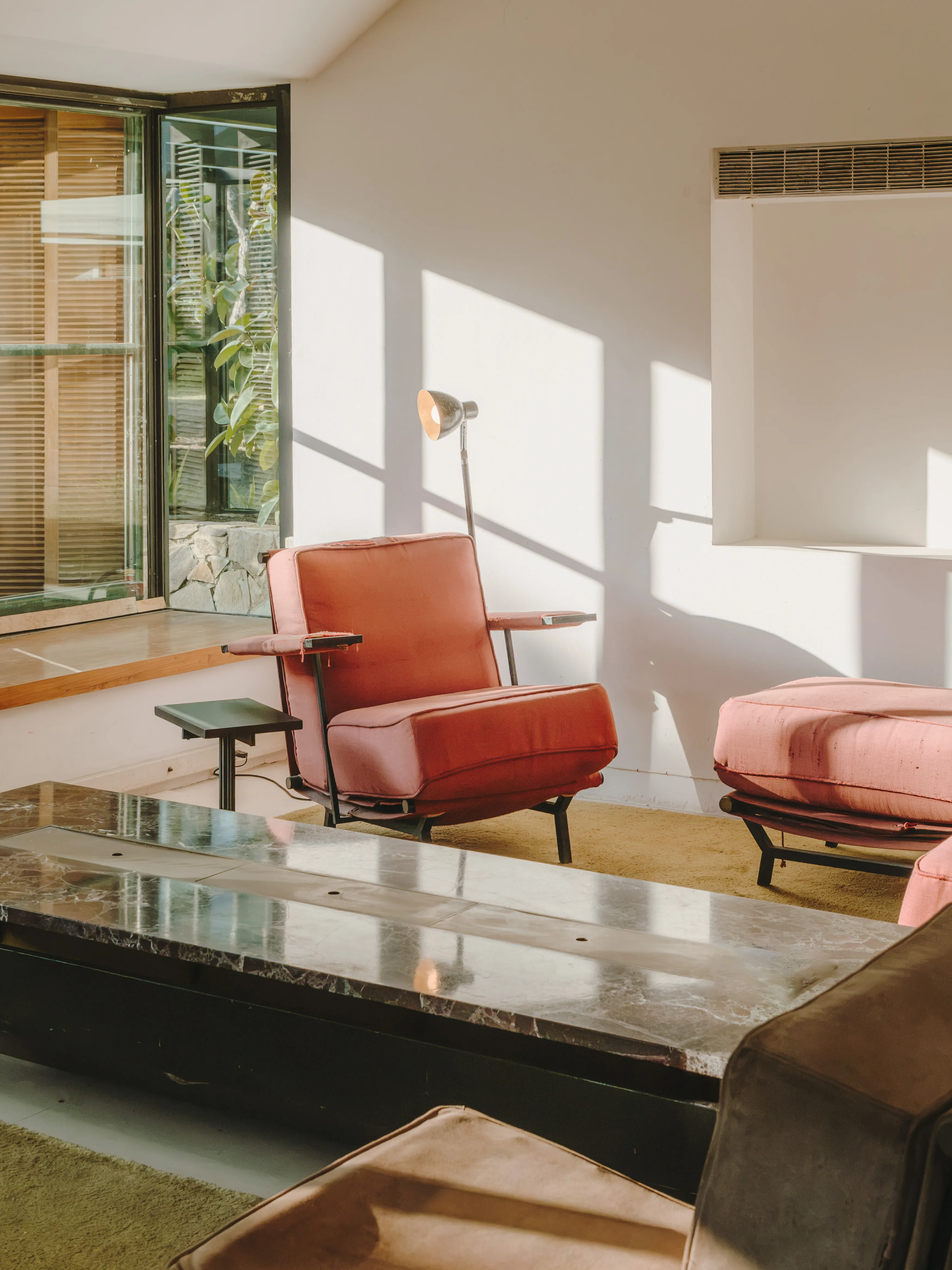Salón luminoso con sillones tapizados en terracota, mesa de mármol y ventana con vistas a la vegetación.