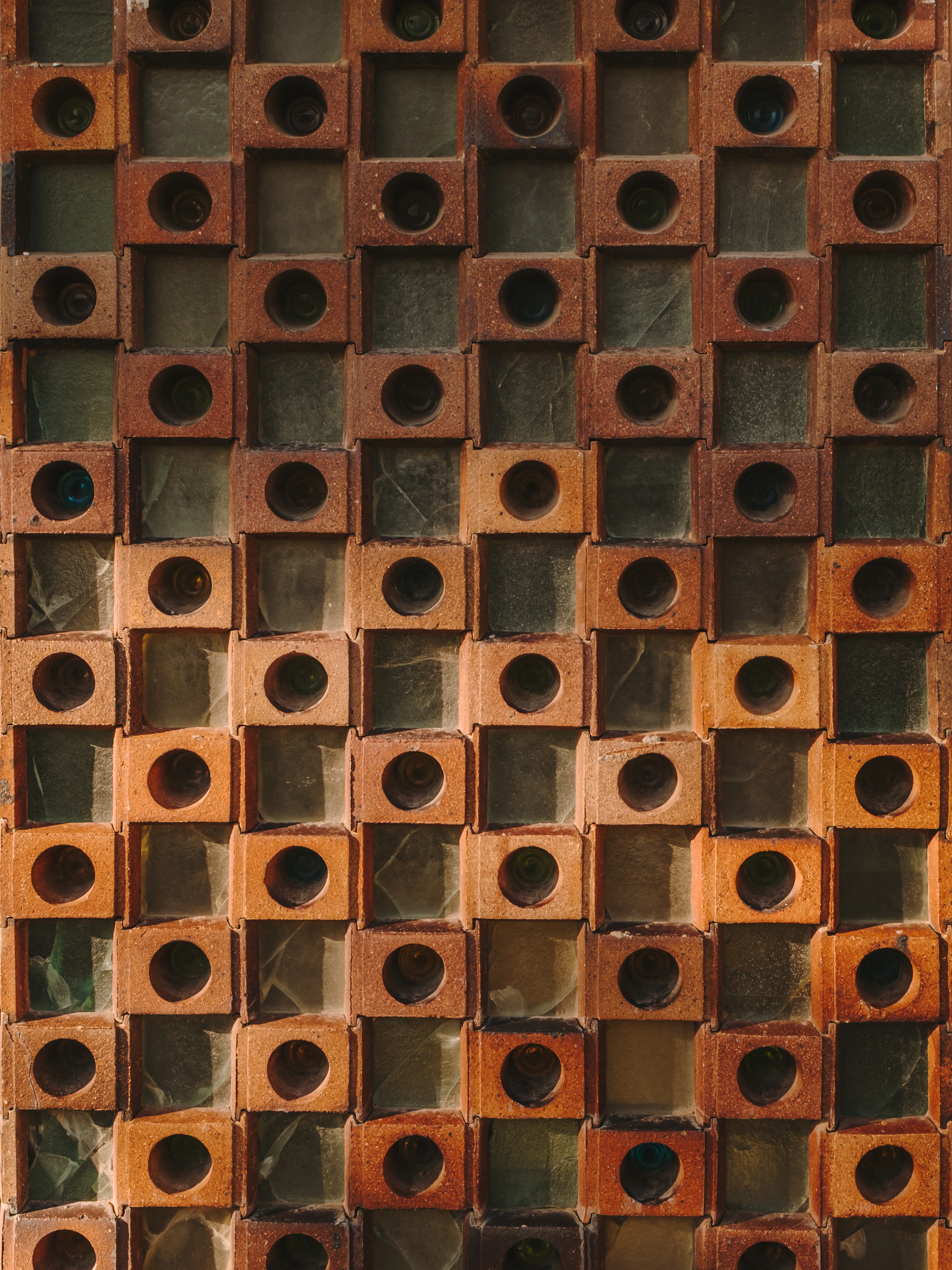 Muro de ladrillo con patrón geométrico de bloques cuadrados y orificios circulares, combinando materiales cerámicos y translúcidos.