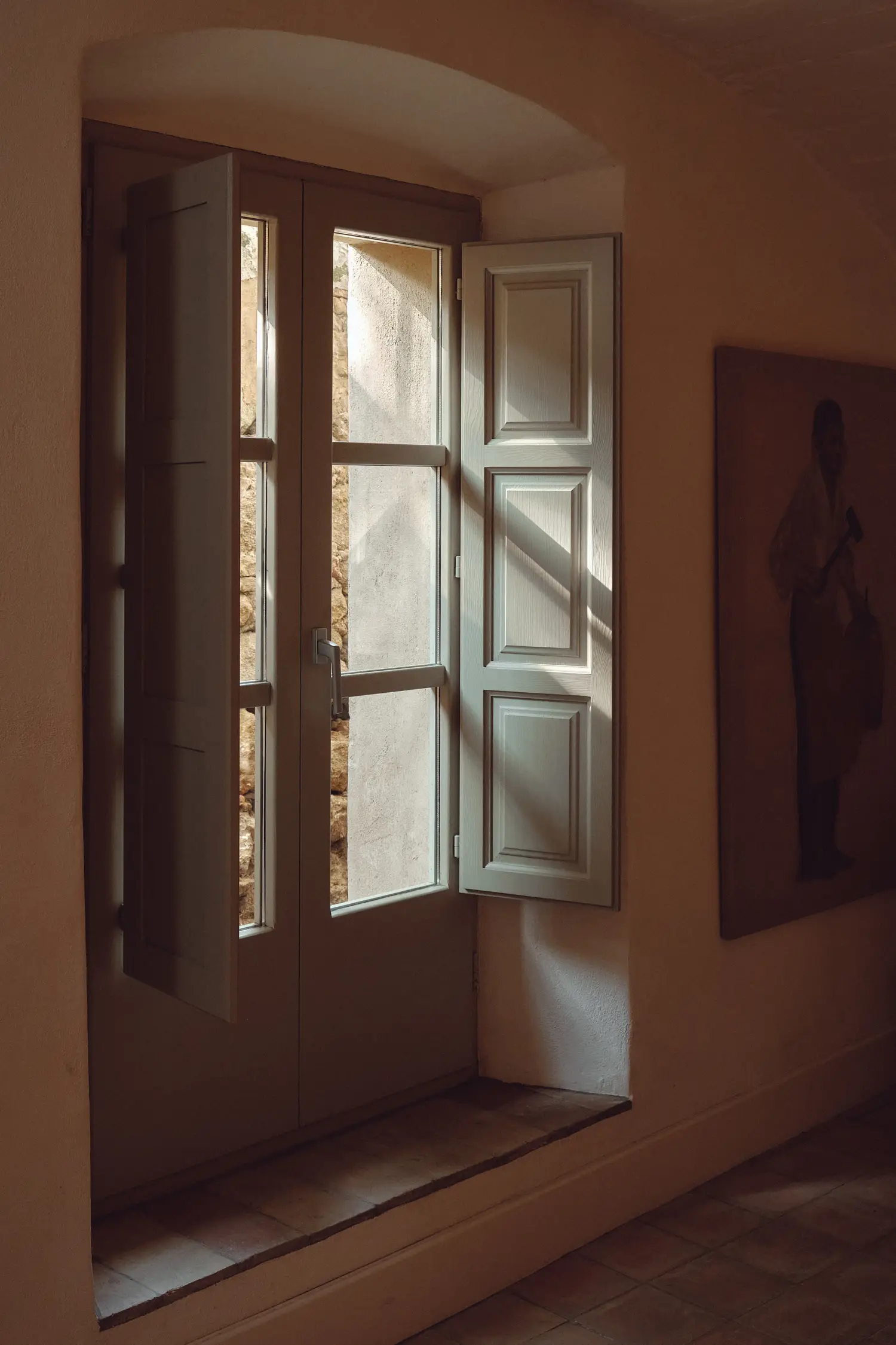 Luz natural inunda una estancia a través de una ventana con persianas de madera abiertas, creando juegos de sombras.